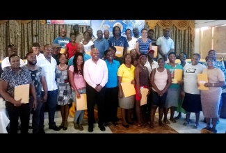 Minister Without Portfolio in the Ministry of Transport, Works and Housing , Hon. Dr. Morais Guy (6th left); and Member of Parliament for Eastern Westmoreland, Luther Buchanan (3rd left), share with proud land owners of Whitehouse, following the handing over of certificates of title on Friday (March 27). Sixty-five residents of the community and 37 others in Galloway district in Whithorn, were presented with titles under the Government’s land titling programme.