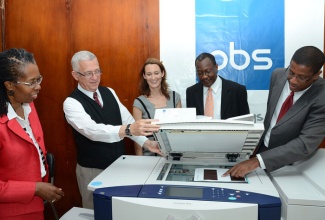 Minister of Education, Hon. Rev. Ronald Thwaites (second left), observes as Senior Accounting Manager, Productive Business Solutions (PBS) Jamaica, Gregory Douet (right), demonstrates how to use the Xerox ColorQube 9303 photocopy machine, during a handing-over ceremony at the Ministry’s Heroes Circle offices in Kingston on Tuesday (August 20). Looking on (from left) are: Permanent Secretary in the Ministry, Elaine Foster Allen; Managing Director, PBS, Melanie Subratie; and Operations Manager, PBS, Paul Reid.