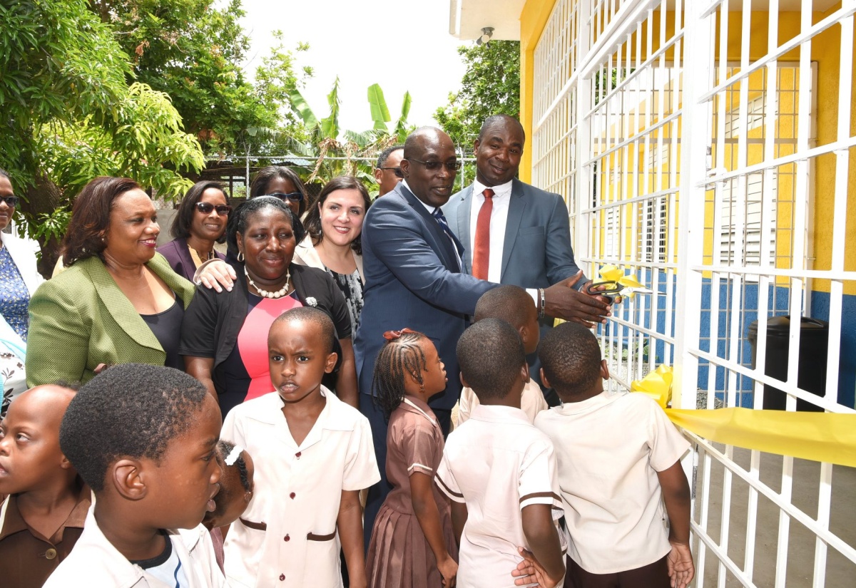 State Minister in the Ministry of Labour and Social Security, Hon. Zavia Mayne (right), is assisted by Minister of Education, Youth and Information, Senator the Hon. Ruel Reid (2nd  right), in cutting the ribbon to officially open the newest building of the Stimulation Plus Early Childhood Development Centre located at Ostend Close, in Rockfort, Eastern Kingston during a ceremony on May 18. Sharing in the moment from left are: Chief Technical Director in the Ministry of Labour and Social Security, Audrey Deer Williams, and Director, Early Stimulation Programme, Antonica Gunter-Gayle. Also pictured are students of the school and other officials.