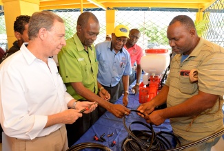 Minister without Portfolio in the Ministry of Industry, Commerce, Agriculture, and Fisheries, Hon. J.C. Hutchinson (second left),  and Clarendon farmer, Anthony Trought (right), examine an irrigation hose at an irrigation and sensitisation seminar for farmers on Wednesday (May 16) at the Denbigh Agricultural Showground in Clarendon. The event was organised by St. Jago Farm and Hardware Supplies (SJFHS) in collaboration with NaanDan Jain Irrigation. Looking on are Regional Manager at NaanDan Jain Irrigation, Thomas Davidovich (left), and Managing Director at SJFHS, O’Brien Johnson.