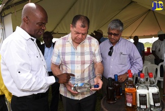 Minister of Industry, Commerce, Agriculture and Fisheries,  Hon. Audley Shaw (centre), examines the label of a Monymusk Rum during a factory tour of National Rums of Jamaica Limited and Clarendon Distillers Limited in Lionel Town, Clarendon, on Thursday (June 14).  With the Minister (from left) are Chief Executive Officer, National Rums of Jamaica, Winston Harrison; and Chairman of the Board of Directors, Komal Samaroo. 

