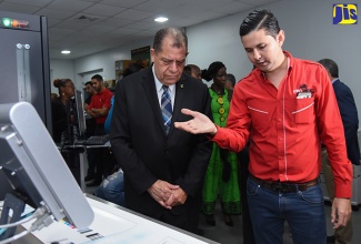 Minister of Industry, Commerce, Agriculture and Fisheries, Hon. Audley Shaw (left), listens as General Manager, Lithographic Printers Limited, Simon Duquesnay, explain how the labelling machine operates, during a tour of the company’s location in downtown Kingston on Wednesday (June 20).  Lithographic Printers is celebrating its 60th anniversary.