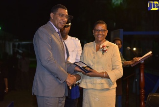 Prime Minister, the Most Hon. Andrew Holness (left) presents Vice-Principal of Calabar Infant, Primary and Junior High School, Claudine Evette Bowen (right), with the Prime Minister’s Medal of Appreciation for Service to Education at the awards ceremony on the lawns of Jamaica House on June 27. Assisting the Prime Minister is Superintendent Michael Morrison.