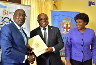 Minister of Tourism, Hon. Edmund Bartlett (centre), presents Minister of Education, Youth and Information, Senator the Hon. Ruel Reid (left),  with a copy of a Memorandum of Understanding (MOU) that will see the implementation of a $100-million Hospitality and Tourism Management Programme in 30 high schools across the island. Both Ministers signed the agreement during a ceremony at Jamaica House on Wednesday (July 11). Also pictured is Permanent Secretary in the Tourism Ministry, Jennifer Griffith.