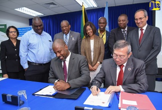 Planning Institute of Jamaica (PIOJ) Director General, Dr. Wayne Henry (left, seated); and International Atomic Energy Agency (IAEA) Deputy Director General for Technical Cooperation, Dazhu Yang (right, seated), sign Jamaica’s new five-year Country Programme Framework (CPF), during a brief ceremony at the PIOJ’s head office in New Kingston on Thursday (August 9). The new CPF will run from 2018 to 2023. Looking on (from left) are Senior Lecturer, Caribbean Institute for Health Research (formerly Tropical Medicine Research Unit) University of the West Indies (UWI), Mona Campus, Professor Asha Badaloo; Permanent Secretary, Ministry of Industry, Commerce, Agriculture and Fisheries; Donovan Stanberry; UWI Mona Campus Principal, Professor Dale Webber; Permanent Secretary, Ministry of Health, Sancia Bennet Templar; Director, Caribbean Institute for Health Research, Professor Marvin Reid; Director General, International Centre for Environmental and Nuclear Sciences (ICENS), Charles Grant; and Section Head, Latin America and the Caribbean, IAEA, Saul Perez Pijuan.