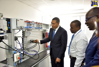 Prime Minister, the Most Hon. Andrew Holness (left), tries out a hydraulic training device in a laboratory at the Festo Authorised and Certified Training (FACT) Centre located at the Caribbean Maritime University (CMU) in Kingston. The occasion was a tour of the facility  following its official opening on Wednesday (September 19). Looking on are Education, Youth and Information Minister, Senator the Hon. Ruel Reid (right); and FACT-certified trainer, Ricardo Hopwood.