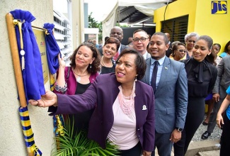 State Minister for Education, Youth and Information, Hon. Floyd Green (second right), observes as Chief Executive Officer (CEO) of the Child Protection and Family Services Agency (CPFSA), Rosalee Gage-Grey (foreground); and Deputy Principal of the University of the West Indies (UWI) Open Campus, Professor Julie Meeks (left), unveil signage at the newly constructed independent living complex for former female wards, at 24 Lady Musgrave Road in St. Andrew on September 18. Looking on are Pro-Vice Chancellor and Principal of UWI Open Campus, Dr. Luz Longsworth (second left); Chargé d'Affaires at the United States Embassy in Kingston, Eric Khant (third left); and Opposition Spokesperson for Foreign Affairs and Foreign Trade, Lisa Hanna (right). 