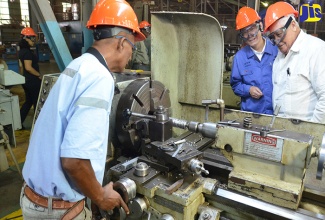 Minister without portfolio in the Office of the Prime Minister, Hon. Mike Henry (right), and former Managing Director at JISCO Alpart Jamaica, Liu Wanxiang (centre), observe mechanic Lenford Samuels at work, during a tour of the plant in in Nain, St. Elizabeth in 2017. 