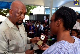 Minister of State in the Ministry of National Security, Hon. Rudyard Spencer (left), presents an inmate at the  Fort Augusta Adult Correctional Centre with a plaque for her achievement in the 2018 Caribbean Secondary Education Certificate (CSEC) examinations. Occasion was an appreciation function at the centre’s location at South Camp Road in Kingston on September 18.