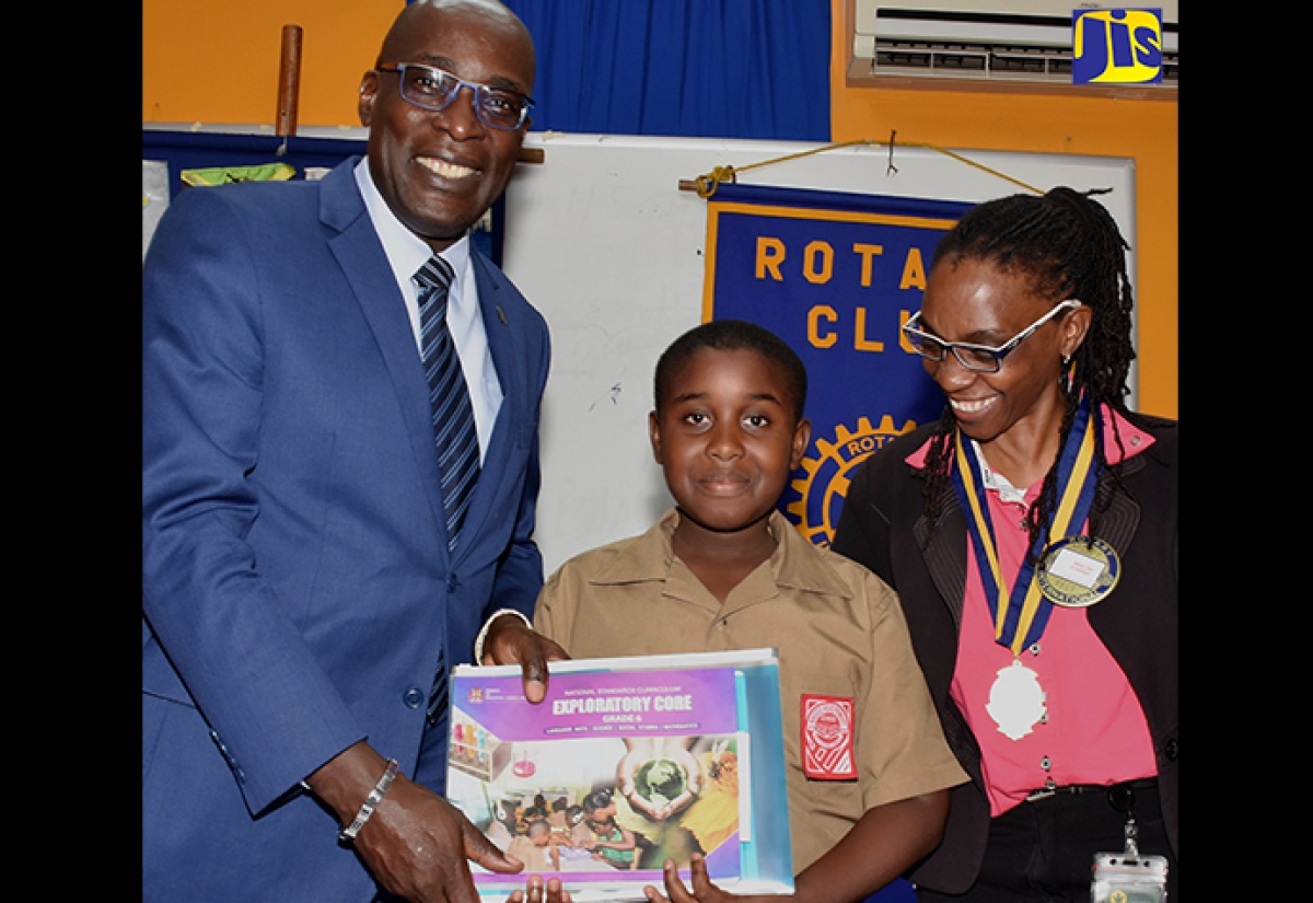 Education, Youth and Information Minister, Senator the Hon. Ruel Reid (left), presents a copy of the National Standard Curriculum and materials of the Primary Exit Profile (PEP) to Naggo Head Primary School student, Rashard Gordon, at a meeting of the Portmore Rotary Club at the Jamaica Employers’ Federation headquarters on Ruthven Road in Kingston on September 19. At right is the club’s President, Vicki Hanson.