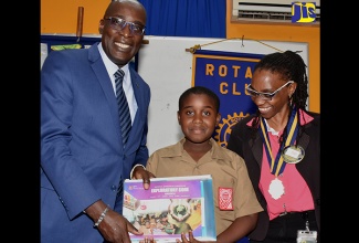 Education, Youth and Information Minister, Senator the Hon. Ruel Reid (left), presents a copy of the National Standard Curriculum and materials of the Primary Exit Profile (PEP) to Naggo Head Primary School student, Rashard Gordon, at a meeting of the Portmore Rotary Club at the Jamaica Employers’ Federation headquarters on Ruthven Road in Kingston on September 19. At right is the club’s President, Vicki Hanson.