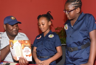 Firefighter of the Jamaica Fire Brigade, Andrade Stoddart (left), shares fire safety tips with students of the Ensom City Primary School - Jazmyne Treasure (centre) and Zhalia Smith. The girls, who are members of their school’s Fire Wardens Club, were in attendance at the launch of Fire and Life Safety Awareness Week at the Spanish Court Hotel in New Kingston on Friday (Oct. 19).