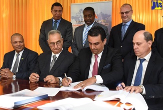 Prime Minister, the Most Hon. Andrew Holness (left, standing); and Transport and Mining Minister, Hon. Robert Montague (centre, standing), look on as Chief Executive Officer of Mexican entity, Grupo Aeroportuario del Pacifico S.A.B. De C.V. (GAP), Raul Revuelta Musalem (second right, seated), signs the 25-year Norman Manley International Airport concession agreement at the Office of the Prime Minister, recently.  Also looking on (seated from left) are President and Chief Executive Officer, Airports Authority of Jamaica (AAJ), Audley Deidrick; AAJ Chairman, Hon. William Shagoury; and Head of GAP  subsidiary, PAC Kingston Airport Limited, Saul Villarreal Garcia; and NMIA Enterprise Team Chairman, Paul B. Scott (standing right). 