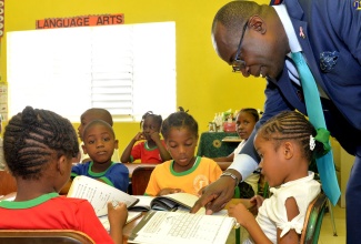 Minister of Education, Youth and Information, Senator the Hon. Ruel Reid (right), assists a grade-one Mona Heights Primary School student with her lesson.  The Minister was taking part in the opening of a new grade-one classroom at the school’s Aralia Drive address in Kingston on Thursday (October 25). 