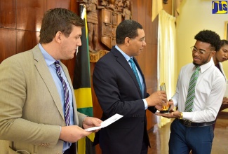 Prime Minister, the Most Hon. Andrew Holness (centre), presents winner of the Jamaica Solar Challenge, Ryan Bent, with a trophy for composing a song to communicate the benefits of solar energy.  Mr. Bent also received a $75,000 cash prize. Occasion was a ceremony to commission solar photovoltaic panels into operation at the Office of the Prime Minister (OPM) on October 16. At left is Director of Solar Head of State, James Ellsmoor. 