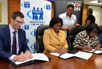 HEART Trust/NTA Managing Director, Dr. Janet Dyer (centre) and (from left),  Executive Director, City and Guilds Group International Division, Jeremy Dadhi, and HEART’s Acting Senior Director for Workforce Development and Employment, Arden Elizabeth Grant, sign a Memorandum of Understanding (MoU) that will facilitate the institutions’ expansion of certification opportunities for Jamaica’s workforce and trainees. The signing took place at HEART’s head office in New Kingston on Friday (December 7). Overseeing the proceedings is Director for HEART’s Business Process Management Unit, Kenesha Campbell.  