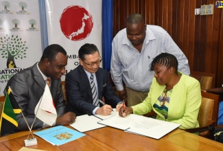 Permanent Secretary in the Ministry of Education, Youth and Information, Dean-Roy Bernard (left), observes as Ambassador of Japan to Jamaica, His Excellency Hiromasa Yamazaki (centre); and Principal of Lyssons Primary School, Evette Bonfield Beecher, sign a grant contract in the amount of US$67,177 (J$8 million) for the purchase of a bus, today (January 22) at the Ministry’s Heroes Circle offices, in Kingston. The grant is being offered through the Government of Japan Grassroots Human Security Project.  Standing is Board Chairman of the school, Cordinal Beckford.