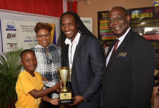 State Minister in the Ministry of Education, Youth and Information, Hon. Alando Terrelonge (second right), presents Holy Family Primary School student, Malique Brown, with the winner's trophy in RISE Life Management Services’ adolescent gambling-prevention jingle competition. The awards ceremony was held on February 27 at the entity's downtown Kingston offices. Sharing the moment are Vice President of Marketing, Communication and Sponsorship, Supreme Ventures Limited, Gail Abrahams (second left); and Executive Director of the Betting, Gaming and Lotteries Commission (BGLC), Vitus Evans. 