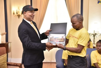 Governor-General, His Excellency the Most Hon. Sir Patrick Allen (left), accepts a photograph of the Special Olympic Jamaica volleyball team from one of the members, Andrew Harris, during a call at King’s House on Friday (March 1).