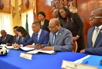 Prime Minister, the Most Hon. Andrew Holness (seated, fourth left), along with Minister of Tourism, Hon. Edmund Bartlett (seated, second right), affix their signatures to a joint venture agreement between the Housing Agency of Jamaica (HAJ) and the China-based Henan Fifth Construction Group, for the construction of 754 affordable units at Rhyne Park in St. James. The signing took place at Jamaica House on Wednesday (April 24). Also pictured (seated, from left) are Chairman of the HAJ, Norman Brown; Business Manager, Overseas Branch, Henan Fifth Construction Group, Qishan Liu; Lawyer, Win-Full Law Firm, Sun Liujin; and Minister without Portfolio in the Ministry of Economic Growth and Job Creation, Senator the Hon. Pearnel Charles Jr. Overseeing the process (standing, from left) are HAJ Directors Fay Hutchinson and Silvester Tulloch; and Permanent Secretary in the Office of the Prime Minister and Ministry of Economic Growth and Job Creation, Audrey Sewell. 