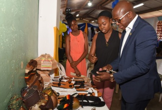 Minister without Portfolio in the Ministry of Economic Growth & Job Creation, Senator the Hon. Pearnel Charles Jr., admires a pair of sandals designed by  Chantal Lewis (centre), at the launch of the Palmer’s Cross Community Development Committee (CDC), in Clarendon, on July 18.  At left is  Ca-Deiva Clarke of Glenmuir High School.