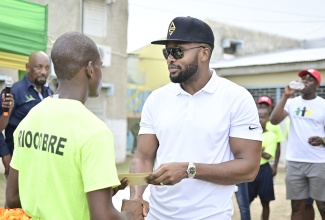 State Minister in the Ministry of National Security, Hon. Rudyard Spencer (left), looks on while Recording artiste, Agent Sasco (right), presents a cash prize of $25,000 to the top male at the recent ‘We Transform’ Sports and Fun Day, held at the Rio Cobre Juvenile Correctional Centre in Spanish Town, St. Catherine