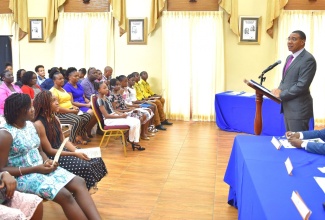 Prime Minister, the Most Hon. Andrew Holness (at podium), addresses attendees at a Primary Exit Profile (PEP) awards function at Jamaica House on Wednesday (Aug 14). Also pictured at the head table is Acting Chief Technical Director in the Office of the Prime Minister (OPM), Damian Cox. The awards ceremony recognised 15 children of OPM and Office of the Cabinet staff members, who were successful in their PEP exams this year. The Prime Minister presented them with book vouchers for back-to-school.