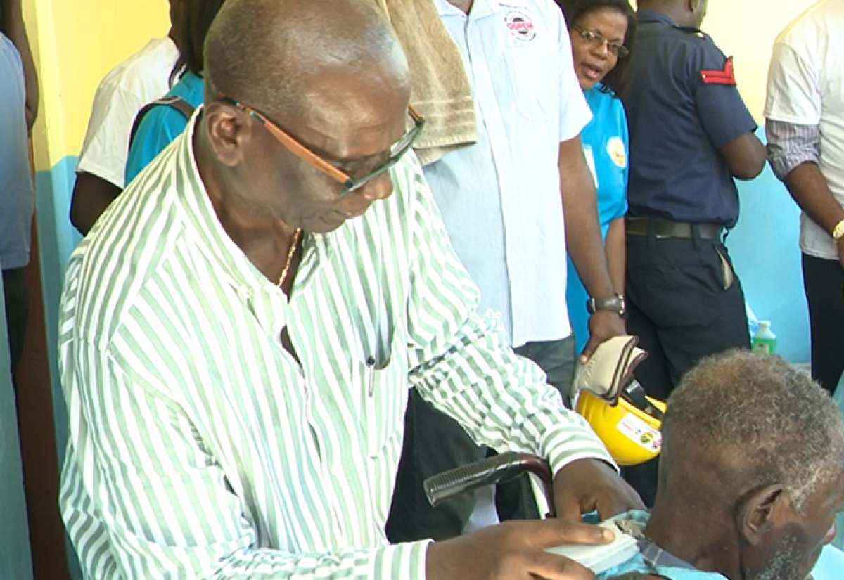 Minister of Local Government and Community Development, Hon. Desmond McKenzie (left), grooms the hair of an elderly resident of the St. Elizabeth Infirmary, during the staging of the Ministry’s second annual Volunteer Day held at the facility in Santa Cruz on Friday (November 15). 