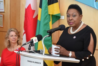 Minister of Culture, Gender, Entertainment and Sport, Hon. Olivia Grange, addresses media representatives at the High Commission of Canada, in Kingston, on Tuesday (December 3). Listening at left is High Commissioner of Canada, Her Excellency Laurie Peters. Occasion was the award of grants to five local organisations to  advance gender equality. 