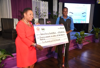 Minister of Culture, Gender, Entertainment and Sport, Hon. Olivia Grange (left), hands over a symbolic cheque for $150,000 to representative of the Jamaica Society for the Blind, Kay-Ann Samuels, at the Stand up, Talk up Public Forum, held at the Courtleigh Auditorium, on Friday (November 29), in New Kingston.