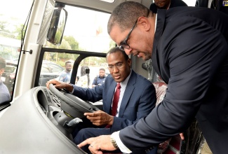 Finance and the Public Service Minister, Dr. the Hon Nigel Clarke (left), listens as Managing Director, Magna Motors Dealership Ltd, Erick Gutierrez, explains the different features of one of the three buses that were officially handed over to the Government Employees Transportation System, during a ceremony held on February 28 at Medallion Hall Hotel in Kingston.