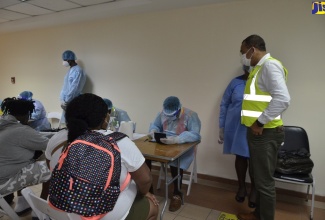 Minister of Health and Wellness, Dr. the Hon. Christopher Tufton (right), observes the health screening and risk assessment process by the health authorities at the Sangster International Airport in Montego Bay, St. James, on Monday (June 15) following the arrival of the first flight into the island as the country reopened its borders to international travellers.