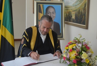 President of the Senate, Senator the Hon. Thomas Tavares-Finson sign the Condolence Book for former Minister of Labour and Social Security, Hon. Shahine Robinson, during the official period of mourning for the late Parliamentarian.