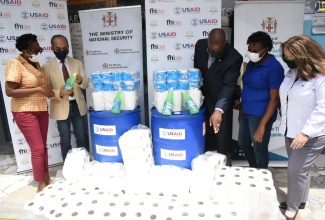 National Security Minister, Hon. Dr. Horace Chang (second left), and Member of Parliament for South West St. Andrew, Dr. Angela Brown Burke (left), look at a bottle of cleaning solution, which was among sanitisation products donated by the United States Agency for International Development (USAID) to Cockburn Gardens Primary and Junior High School for its summer programme. The handover took place at the school in Kingston on July 15. Also pictured are USAID Country Representative, Jason Fraser (third right); Principal of the school, Dr. Patricia Kinglocke Findley (second right) and USAID representative, Morana Krajnovic. 