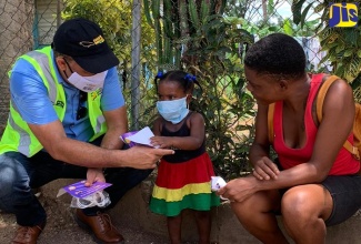 Minister of Health and Wellness, Dr. the Hon. Christopher Tufton, interacts with a toddler in the Bottom Town community in Clark's Town, Trelawny, on Friday (July 24), while her mother looks on. Occasion was a sensitisation walk in the community, which has two imported cases on the coronavirus (COVID-19).