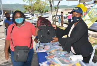 Regional Administrator, Western Parks and Markets (WPM) Waste Management Limited, Karen Clayton (right), hands over a shool  bag to street sweeper, Tamara Chambers, during a book drive and back-to-school treat, staged by the entity, at the Sagicor Commercial Complex in Montego Bay on Friday (August 21).