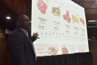 Founder/Chief Executive Officer, OEXONE, Robert Kibo Thompson, points to a chart that highlights examples of how the OEXONE online platform will operate, at its launch on July 15, at the Jamaica Conference Centre in downtown Kingston.