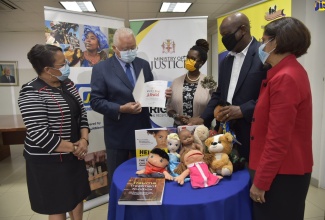 Justice Minister, Hon. Delroy Chuck (second left), peruses a book during the handover of play therapy tools for children by the Jamaica National (JN) Foundation to the Ministry’s Victims Services Division (VSD) on Friday (October 16). Others (from left) are: Chief Technical Director in the Ministry, Grace-Ann Stewart-McFarlane; General Manager, JN Foundation, Onyka Barrett-Scott; Director, VSD, Osbourne Bailey; and Permanent Secretary in the Ministry, Sancia Bennett-Templer.