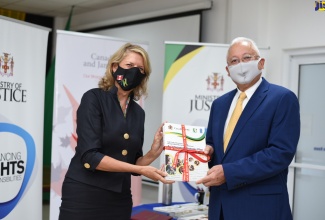 Canadian High Commissioner to Jamaica, Her Excellency Laurie Peters (left) hands over a copy of the Witness Care Strategy and Action Plan to Minister of Justice, Hon. Delroy Chuck, at the Ministry's offices in Kingston on Wednesday (October 28). 
