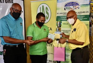 Minister of Agriculture and Fisheries, Hon. Floyd Green  (centre), looks at one of the vouchers that St. Jago Farm and Hardware Supplies Limited  is making available to farmers who have been impacted by the coronavirus (COVID-19) pandemic. Managing Director of the company, O'Brien Johnson  (right), handed over the vouchers during a ceremony at the Denbigh Showground in Clarendon on Thursday (November 26) for the presentation of $7.5 million in support to farmers​.  At left is Chief Technical Director in the Ministry, Michael Pryce.

