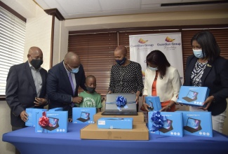 Minister of Education, Youth and Information,  Hon. Fayval Williams (third right), shows a laptop to student, Clan Carty Primary School, Dellano Stewart (third left), at a handover ceremony hosted by Guardian Life Limited, at Trafalgar Road in Kingston on Wednesday (February 10). Sharing in the moment are (from left): Senior Teacher, Clan Carty Primary, Donovan Vincent; Member of Parliament, South East St. Andrew, Julian Robinson; Vice President, Business User Support Services and Special Projects, Guardian Life, Kelsa-Marie Pinnock Daubon; and Director, Donor & Partnership Management, ‎National Education Trust, Latoya Harris. 