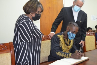 Newly-elected leader of the Accompong Maroons, Chief Richard Currie signs the Parliament's Official Visitors' Book while Senator the Hon. Thomas Tavares-Finson, President of the Senate and Hon. Marisa Dalrymple-Philibert, Speaker of the House of Representatives, look on. Chief Currie paid a courtesy call on the Parliaments' Presiding Officers on Wednesday. During the visit the President and Speaker discussed Chief Currie's plans for agricultural and tourism development in Accompong.  
