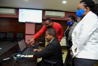 Minister of Agriculture and Fisheries, Hon. Floyd Green (seated), tries out the Ministry's new online Customer Feedback System, while Acting Computer Applications Manager and developer of the website, Ricardo Gayle (second left), points out some of the features. Occasion was the virtual launch of the system on Wednesday (May 26). Looking on are ​Acting Director of Customer Service at the Ministry, Taniesha Clarke (second right); and Acting Manager for Customer Care, Jamila Francis.