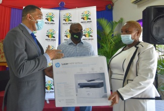 Prime Minister, the Most Hon. Andrew Holness (left), hands over a printer to Principal, McCauley Primary School, Claudia Byer (right), at Harmony Hall Gospel Church on Corletts Road in St. Catherine South Central, on June 18. Sharing the moment is Member of Parliament for the area, Dr. Andrew Wheatley.