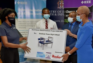 Education, Youth and Information Minister, Hon. Fayval Williams (right), and Chair, Institute of Electrical and Electronics Engineers (IEEE) Jamaica Women in Engineering Affinity Group, Charlene Brown (left), display a photo of one of 350 desk shields being donated by the organisation to the Denham Town High School in Kingston. The occasion was a symbolic handover ceremony for the shields at the Ministry’s offices in Kingston on Friday (June 25). Looking on are Denham Town High student, Taquan Graham (2nd left), and Acting Principal, Donovan Hunter. 