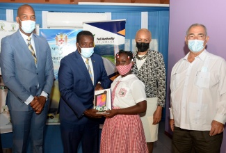 Minister of Transport and Mining, Hon. Robert Montague (second left), presents a tablet to grade-four Portsmouth Primary School student, Sarah Malcolm. Occasion was a ceremony held at the Ministry in Kingston on Tuesday (June 29), to hand over 50 tablets donated by the Toll Authority of Jamaica to the school based in Portmore, St. Cathrine.  Looking on (from left) are Member of Parliament for St. Catherine South Eastern, Robert Miller (left); Minister of Education, Youth and Information, Hon. Fayval Williams; and Custos of Clarendon and Board Chairman of the Toll Authority of Jamaica, William Shagoury.

