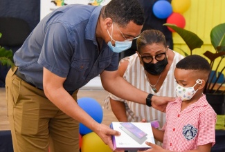 Prime Minister, the Most Hon. Andrew Holness (left), presents student of Clark’s Town Primary School in Trelawny, Aiden Blake, with a tablet computer, during a ceremony at the school on Friday (July 2). Sharing in the occasion is Member of Parliament for Trelawny Southern, Marissa Dalrymple Philibert. The Prime Minister donated 40 tablets to students from seven primary-level schools in Southern Trelawny, through his Positive Jamaica Foundation.