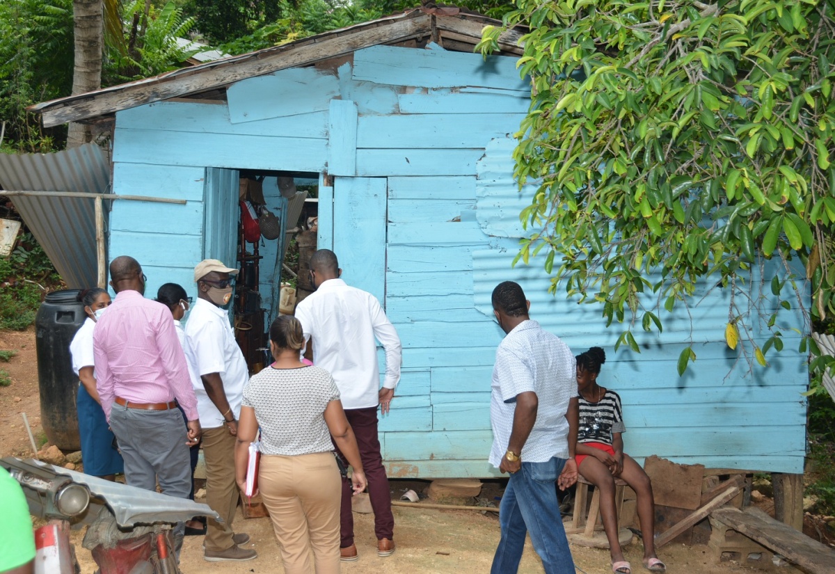 Minister of Local Government and Rural Development, Hon. Desmond McKenzie (fourth left), and stakeholders of the Delveland community in Westmoreland, look at a one-bed board house, which is to be replaced by a two-bedroom unit for a poor family of six. The visit took place on July 15. 