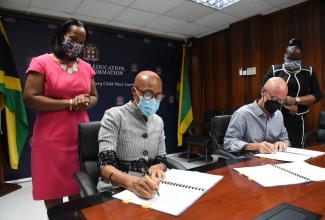 Education, Youth and Information Minister, Hon. Fayval Williams (left) and President of the Rockhouse Foundation (right), sign a Memorandum of Understanding (MOU) to facilitate the expansion of the Savanna-la-Mar Inclusive Infant Academy, in Westmoreland, at the Ministr in Kingston,  on July 13. Observing is Acting Chief Education Officer in the Ministry, Dr. Kasan Troupe (standing, left) and Acting Permanent Secretary, Dr. Grace McLean.

