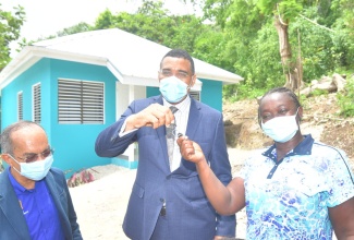 Prime Minister, the Most Hon. Andrew Holness, hands over the keys to a new three-bedroom house built under the Government's new Social Housing Programme to resident Marva Mason (right), during a ceremony in Quarry, St. James, on Wednesday (July 14). Looking on is Deputy Prime Minister & Minister of National Security, Hon. Dr. Horace Chang.    Yhomo Hutchinson Photos

